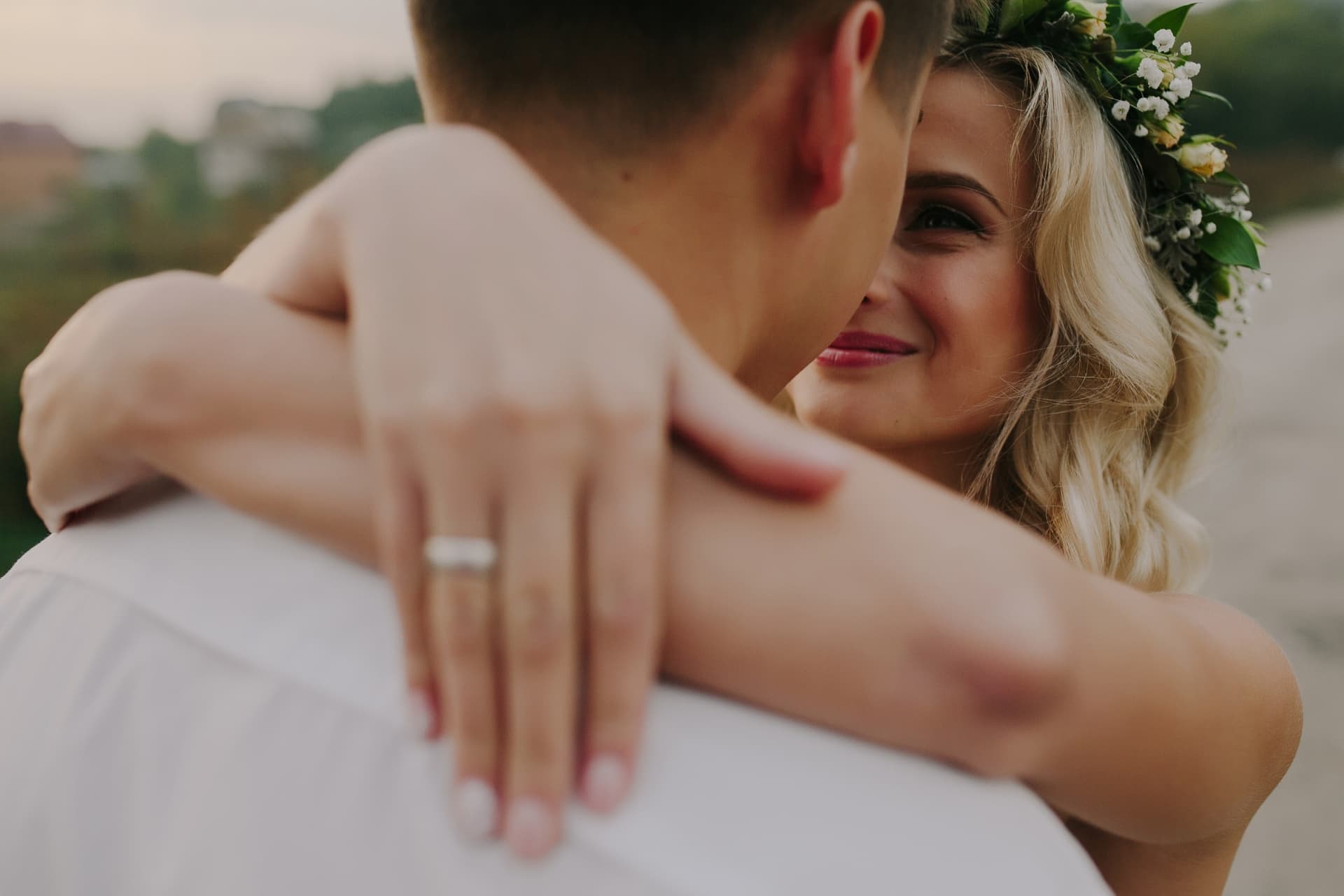 A bride with a flower crown embracing her partner outdoors